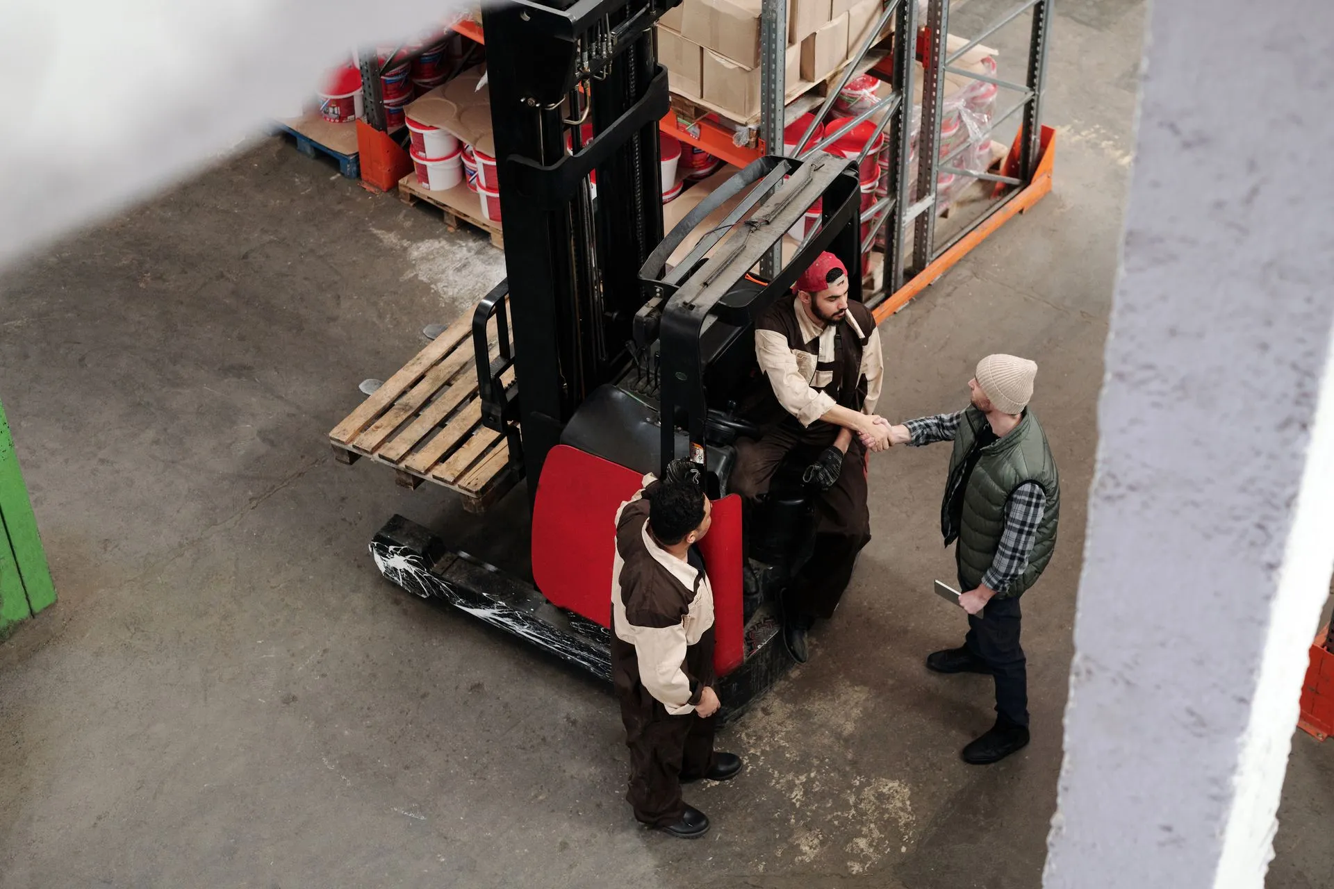 Two logistics workers shaking hands in a warehouse aisle